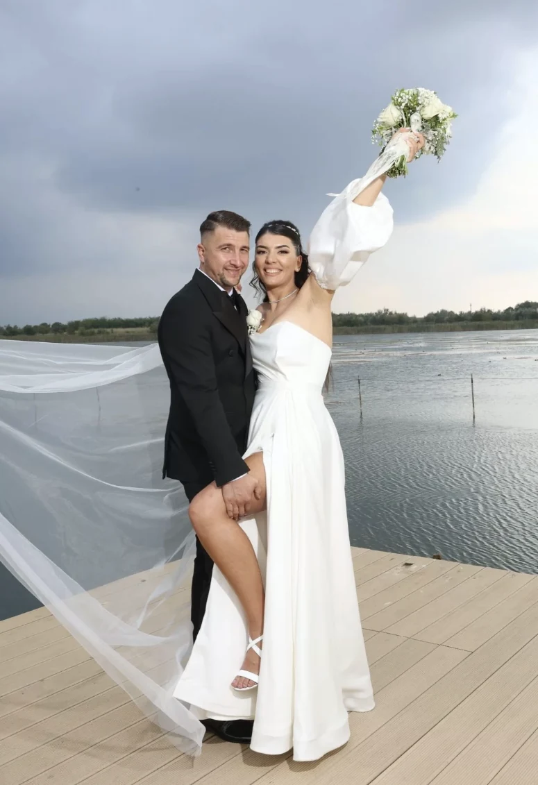 Miresa ridică buchetul, cu voalul purtat de vânt, pe un ponton